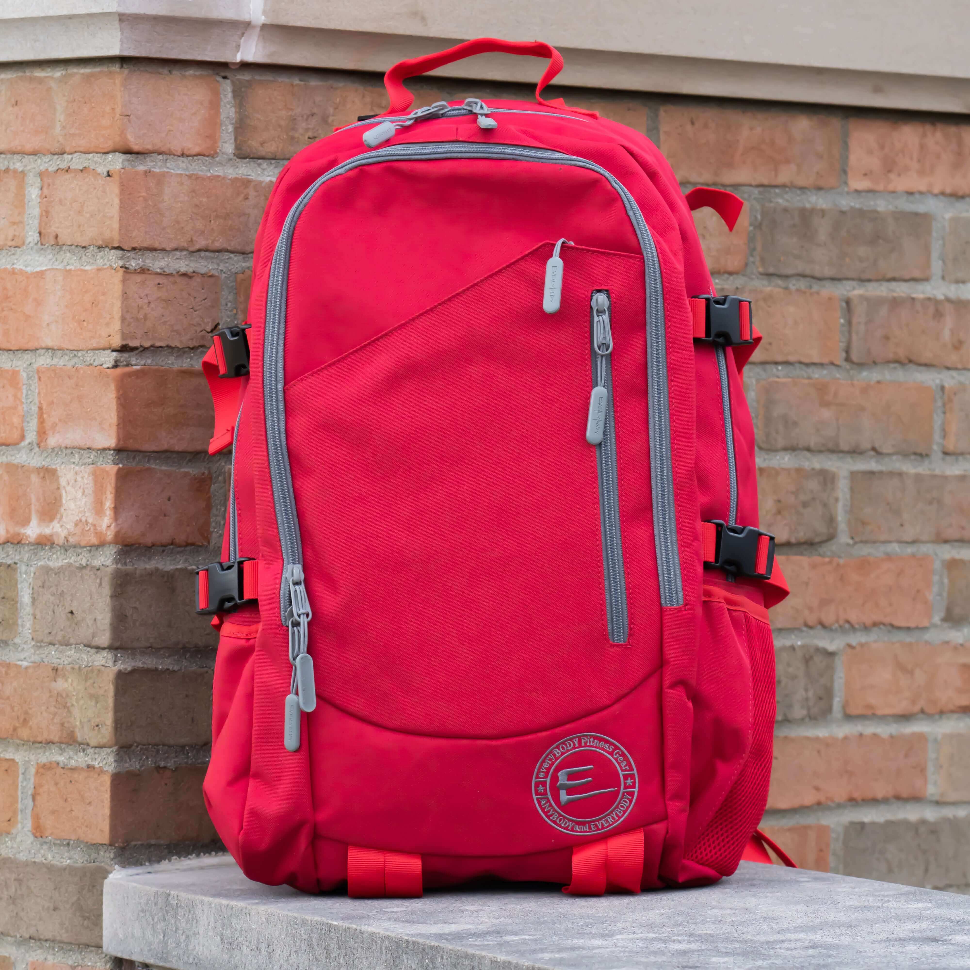 30L Red Backpack with Cup Holders sitting near a brick wall.