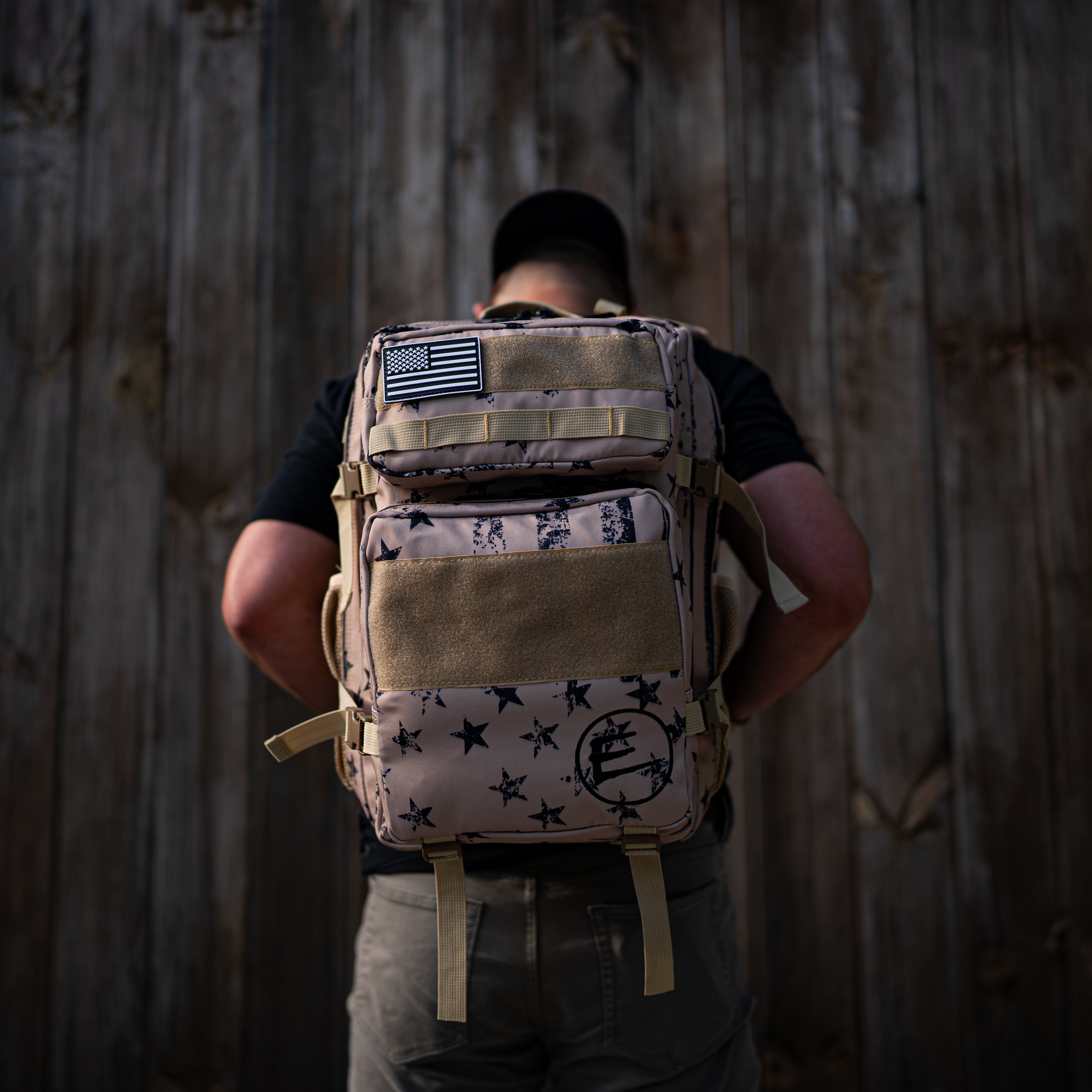 Person wearing a tactical backpack with star pattern and American flag patch against a wooden background.
