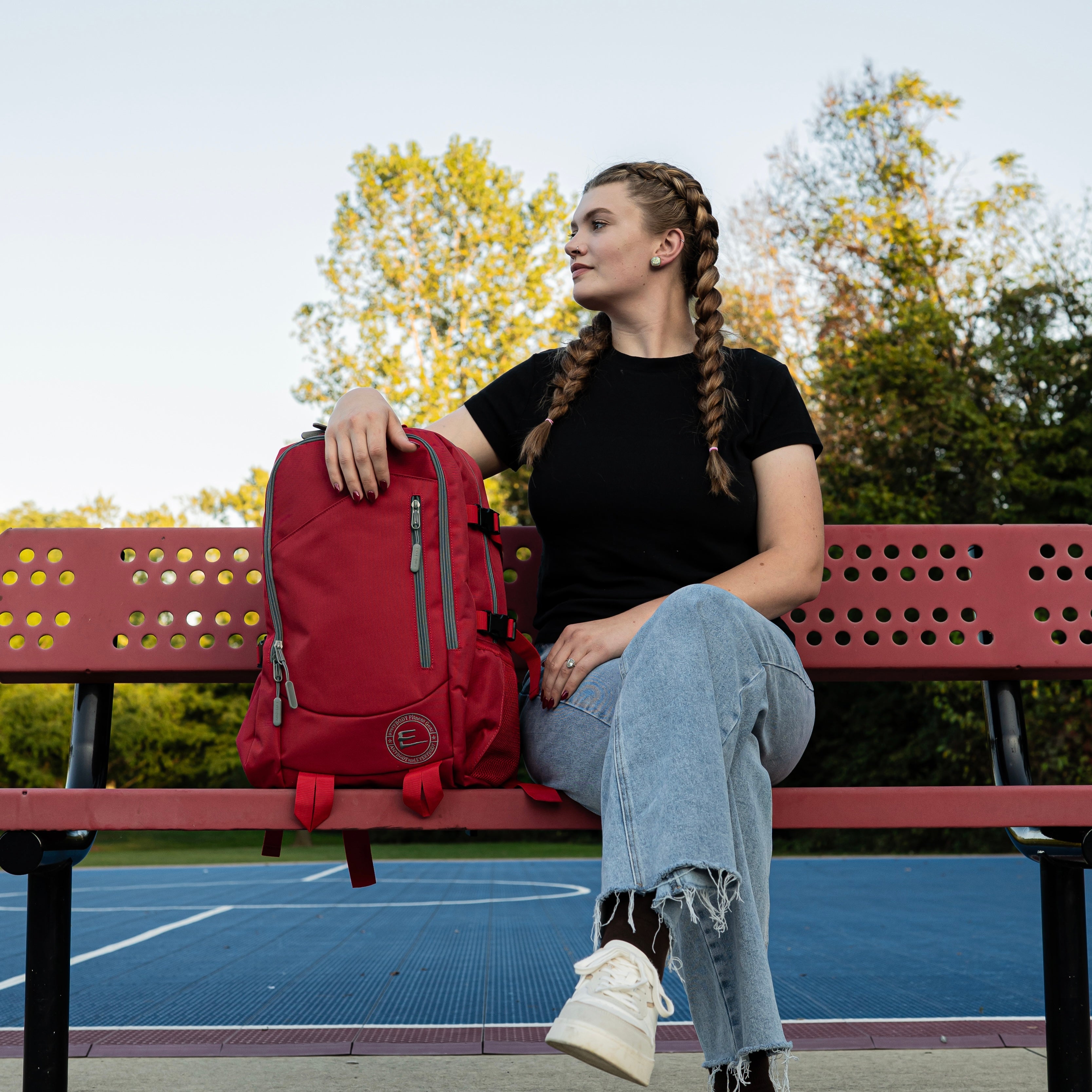 30L Red Backpack sitting on a bench next to a girl wearing a black shirt and blue jeans, outdoors.