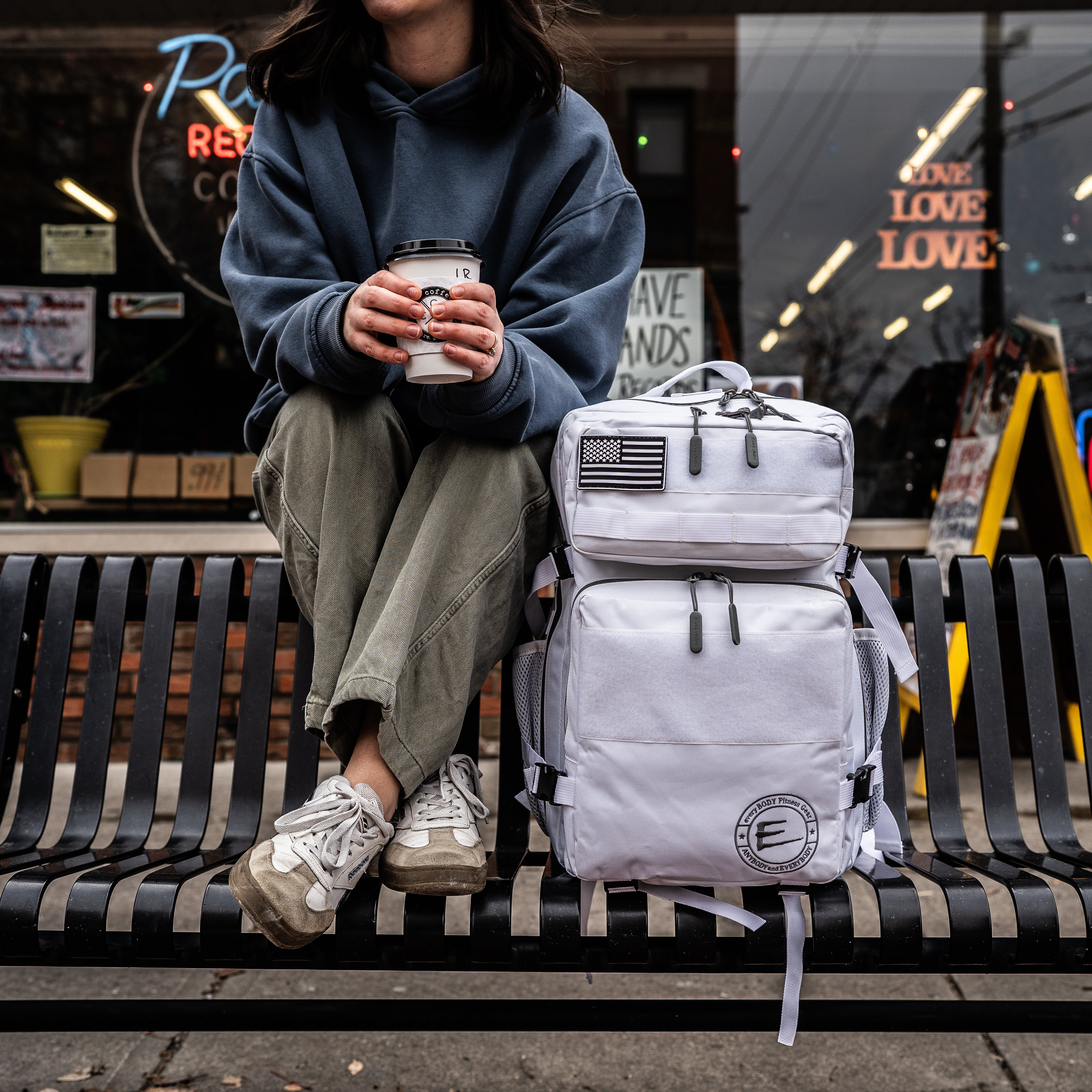 45L White Backpack with Cup Holders, sitting outside on a black bench, showcasing the front view of the bag.